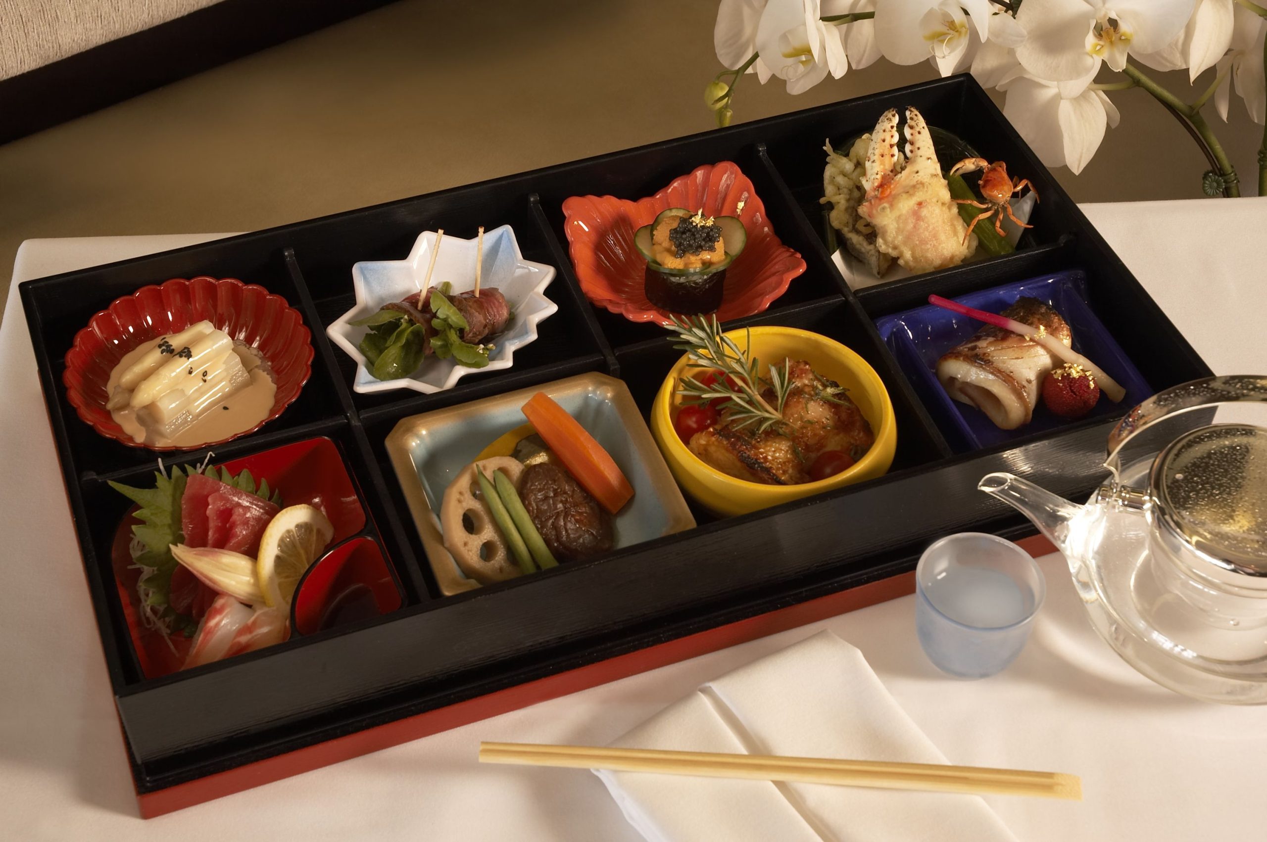 Lacquered box of eight small seasonal dishes beside white orchids