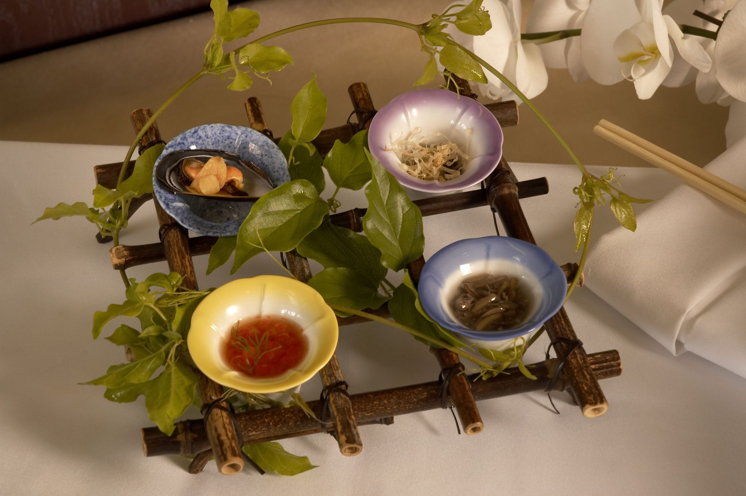 Four small appetizer bowls on a bamboo stand woven with green vines
