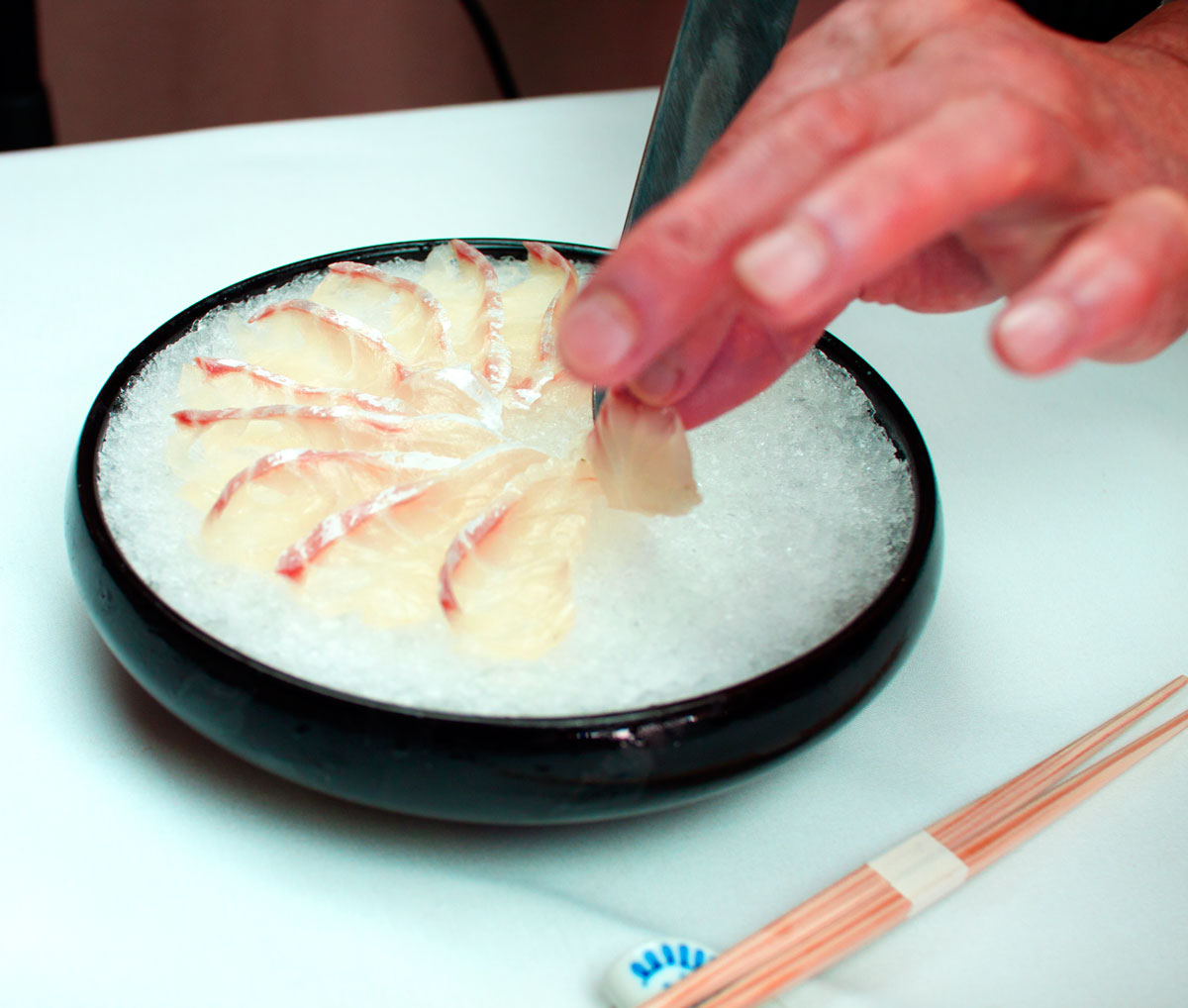 Chef plating thinly sliced sashimi over ice